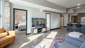 A modern apartment with a living room, kitchen, and bedroom. It features a large window, a ceiling fan, and a kitchen island.