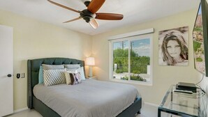 Une chambre à coucher avec un lit, un ventilateur de plafond, une fenêtre donnant sur un beau paysage et une table de chevet avec une lampe.