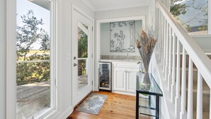 A hallway with white doors, a glass door leading outside, a small kitchen area, and a staircase with white railings.