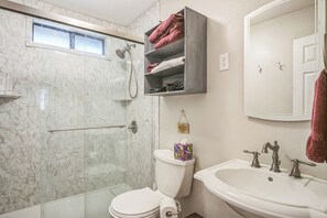 A bathroom with a glass shower enclosure, a toilet, a sink with a mirror, and a towel rack with towels.