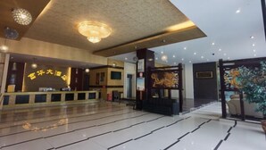 A hotel lobby with a reception desk, a large chandelier, and a decorative wall with a lion sculpture. - Fuhua Hotel (Pingwu)