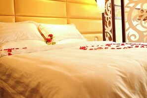 A bed with white linens and red rose petals, a decorative headboard, and a window with a view. - Fuhua Hotel (Pingwu)