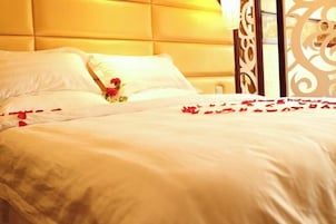 Una cama con sábanas blancas y pétalos de rosa roja, un cabecero decorativo y una ventana con vistas.