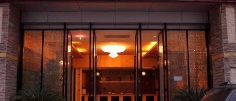 A hotel entrance with a reception desk, glass doors, and a sign above.