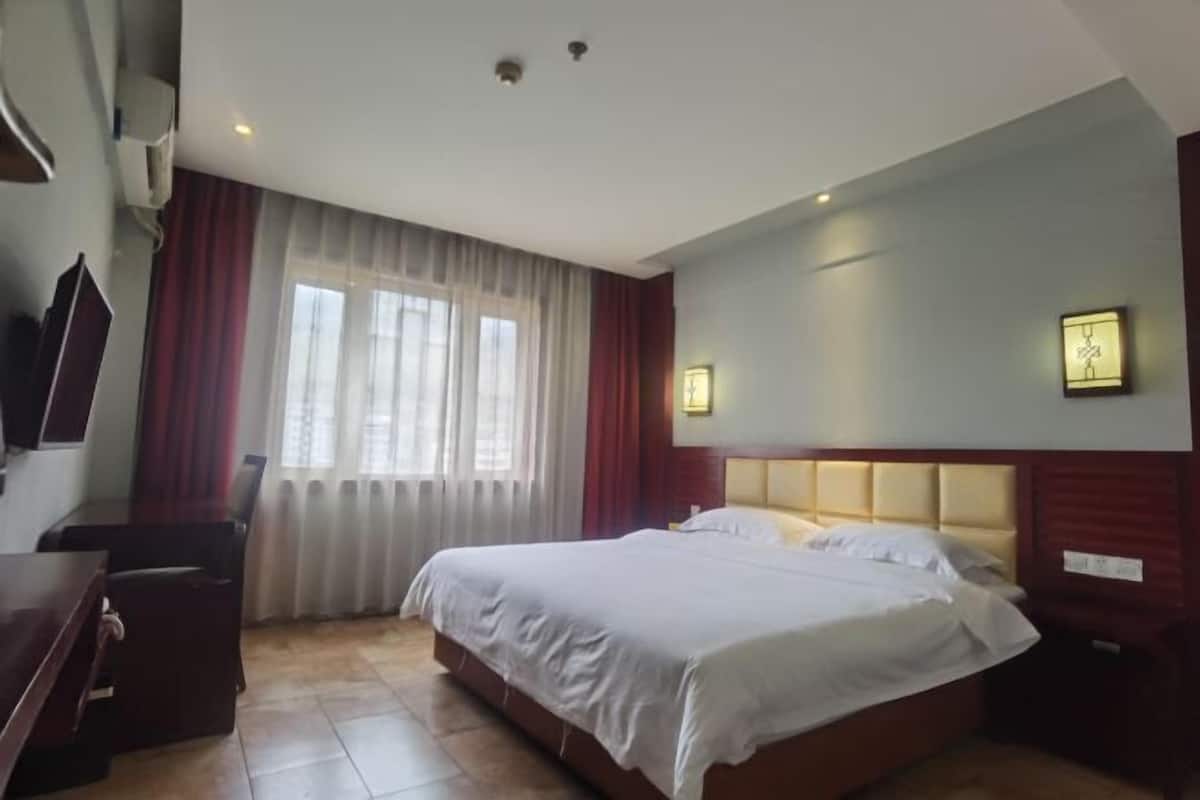 Habitación de hotel con cama, escritorio, silla, televisor y ventana con cortinas.