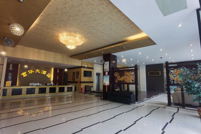 A hotel lobby with a reception desk, a staircase, and a large plant.
