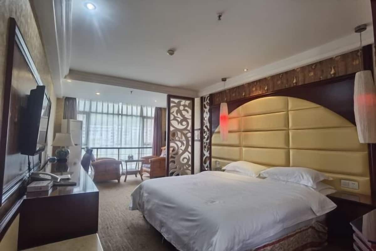 Habitación de hotel con una cama grande, un escritorio con teléfono, una silla y vistas al exterior a través de ventanas amplias.