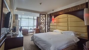 A hotel room with a large bed, a desk with a telephone, a chair, and a view of the outside through large windows. - Fuhua Hotel (Pingwu)