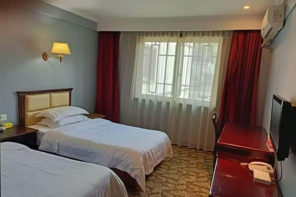 Una habitación de hotel con dos camas, un escritorio con teléfono, una lámpara y una ventana con cortinas.