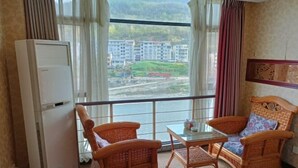 A room with wicker furniture, a glass table, and a view of buildings and greenery through large windows. - Fuhua Hotel (Pingwu)