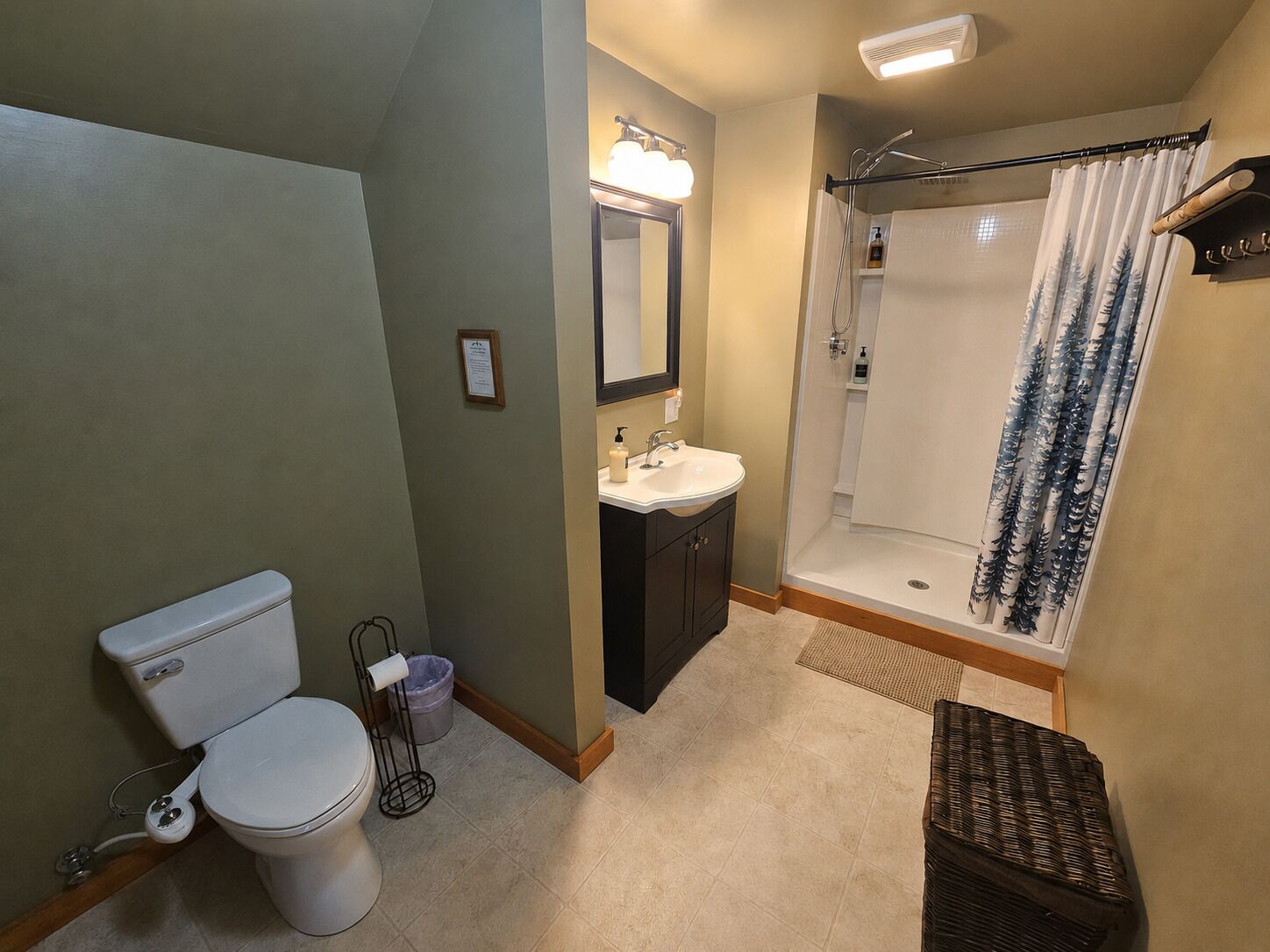 A bathroom with a toilet, sink, mirror, shower, and a small wicker basket.