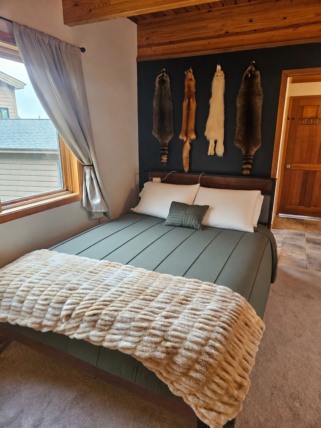 A bedroom with a bed, a window with curtains, a wall with fur pelts, and a wooden door.