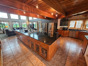 A spacious kitchen with a large island, wooden cabinets, and a view of the outdoors. - Bear Mountain Lodge (Robbinston)