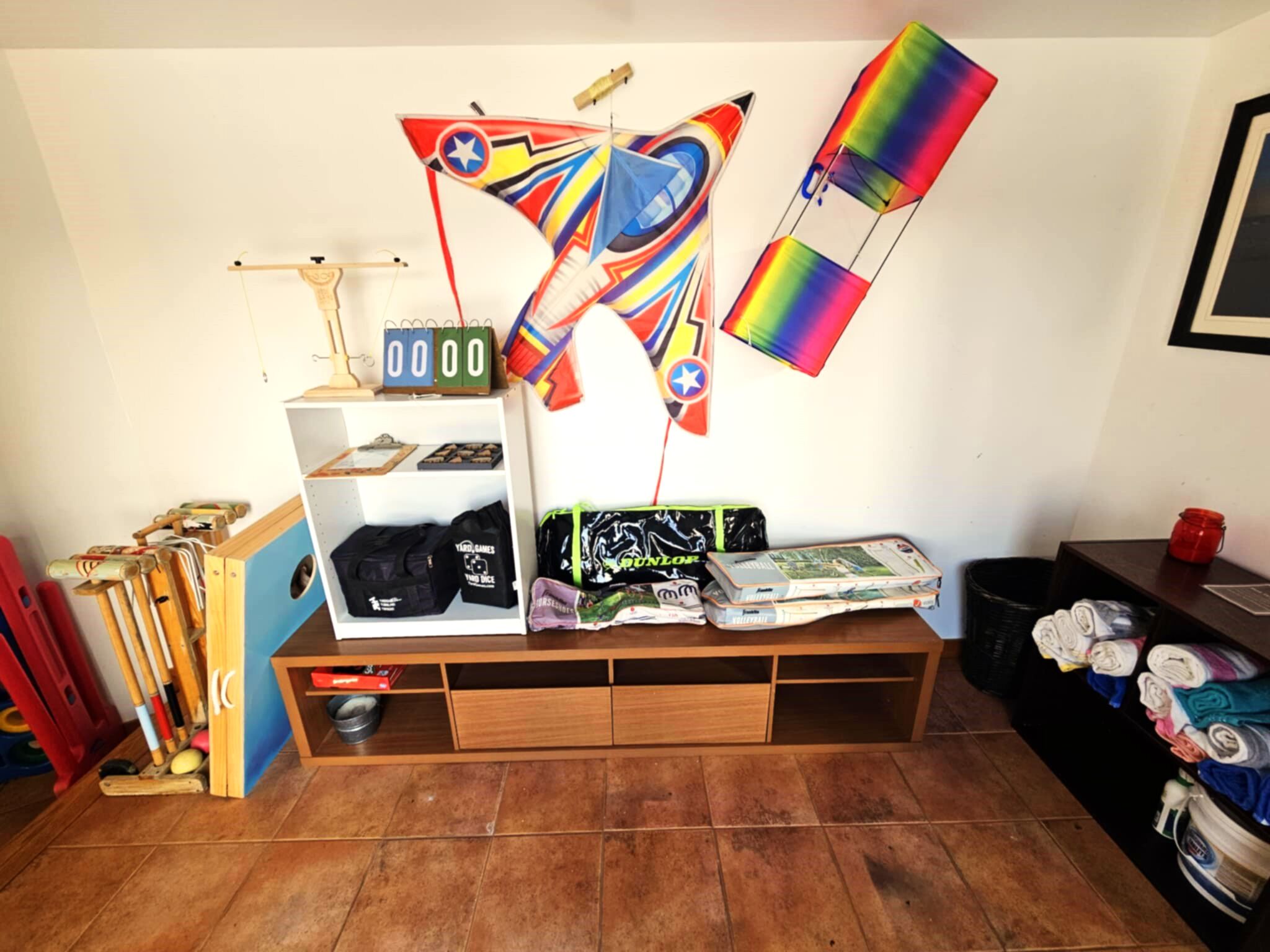 Una habitación con un banco de madera, estante con diversos objetos, un calendario y un pequeño cubo de basura.