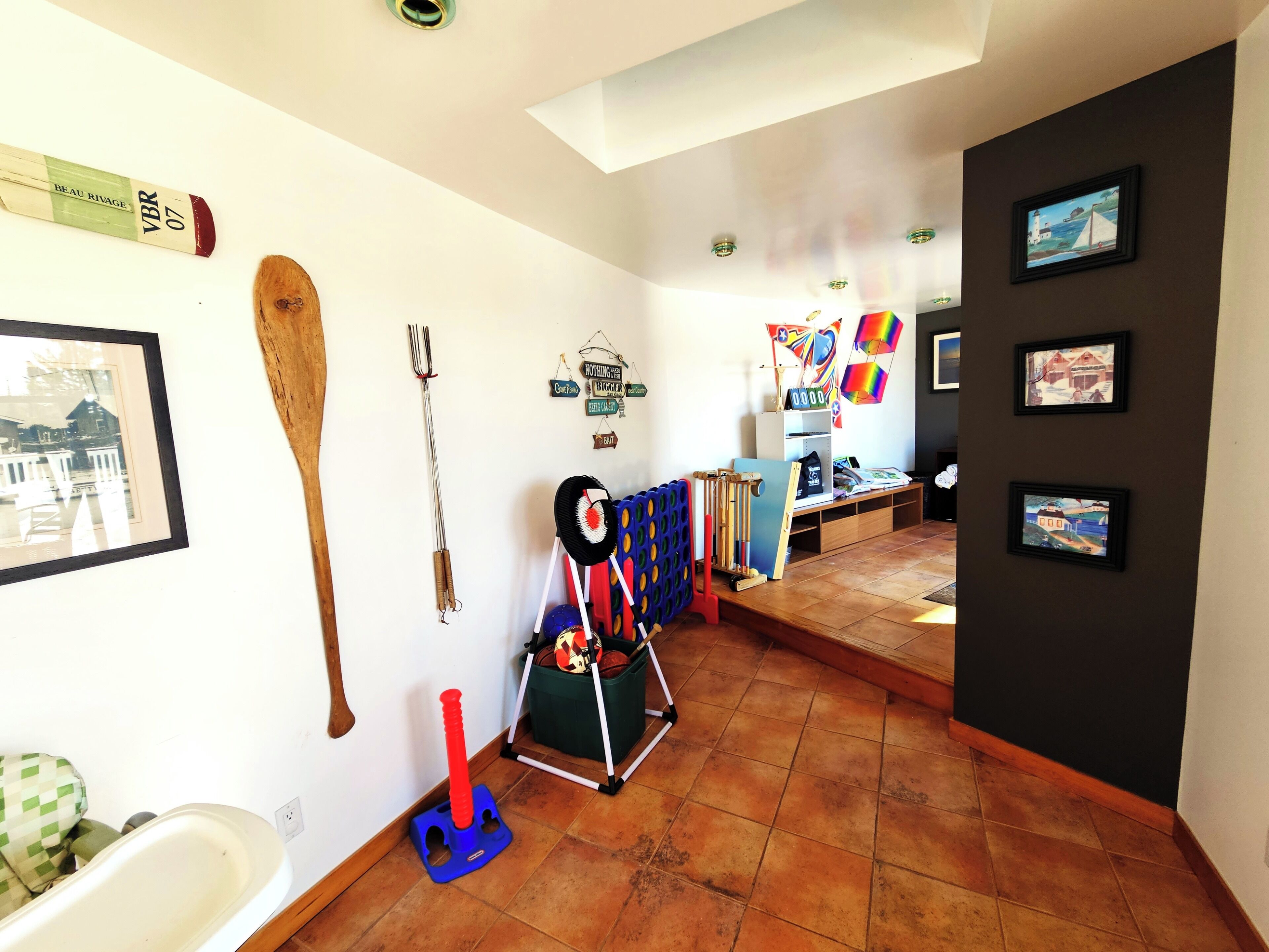 Un pasillo con pared blanca, suelo de madera y techo con tragaluz. Se observan cuadros enmarcados en la pared y un perchero con diversos objetos.
