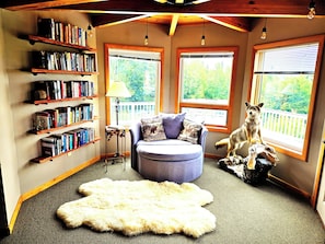 A cozy reading nook with bookshelves, a comfortable chair, a fluffy rug, and a dog statue. - Bear Mountain Lodge (Robbinston)