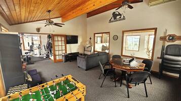 A cozy lodge interior with a foosball table, a dining area, and a gym visible through an open door.