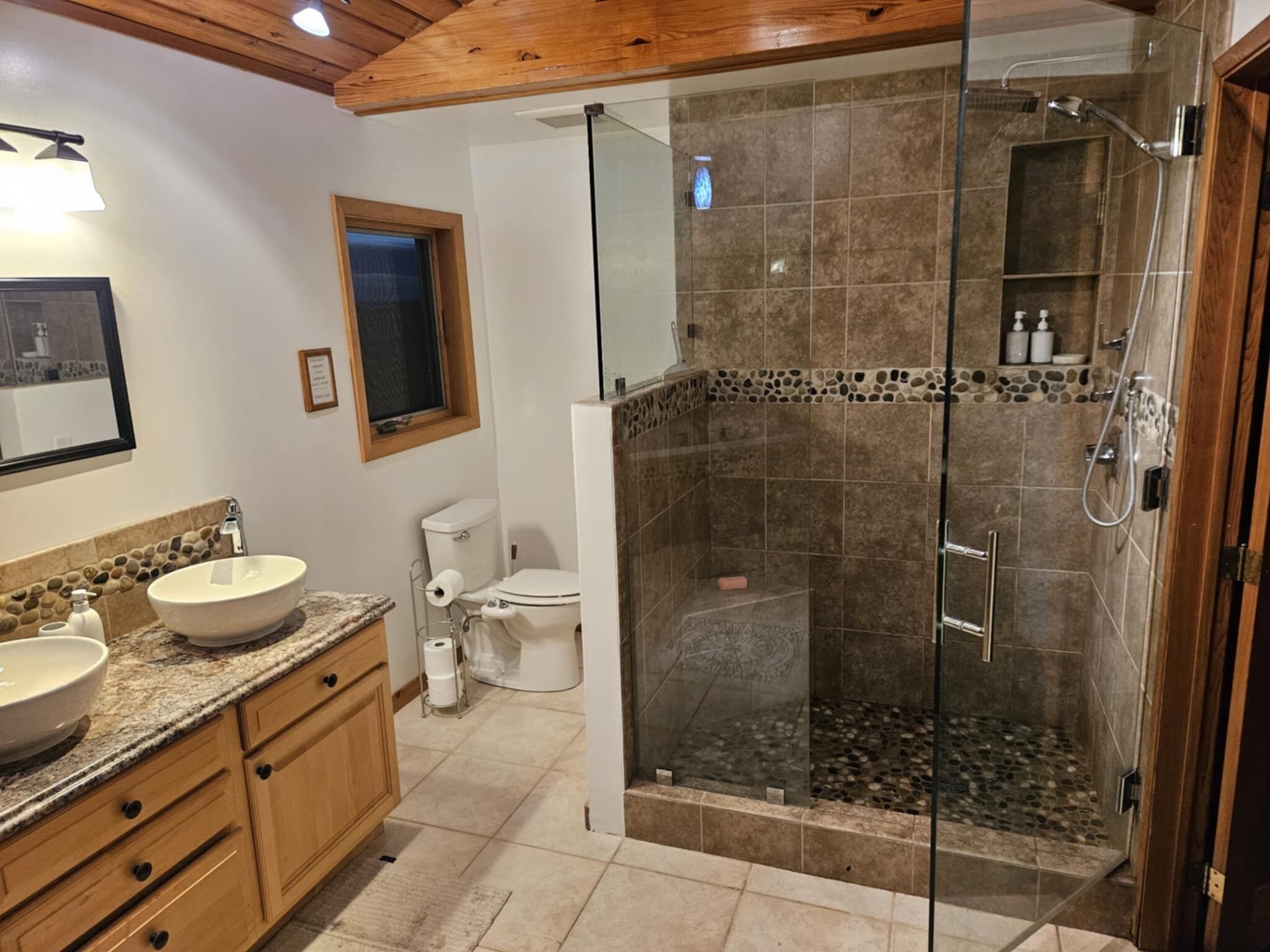 A bathroom with a glass-enclosed shower, a sink with a marble countertop, and wooden cabinets.