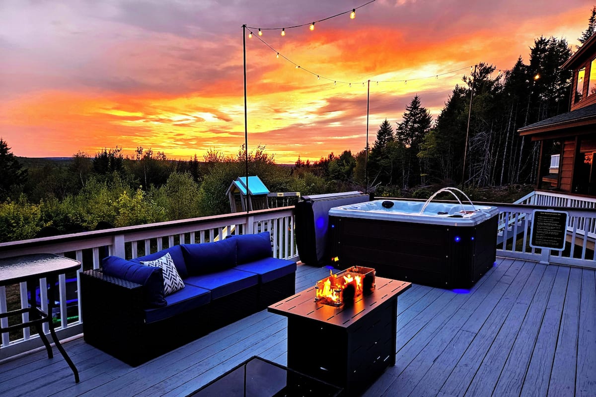A deck with a sofa, a glass table, and a hot tub.