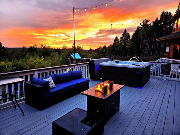 A deck with a sofa, a glass table, and a hot tub. - Bear Mountain Lodge (Robbinston)