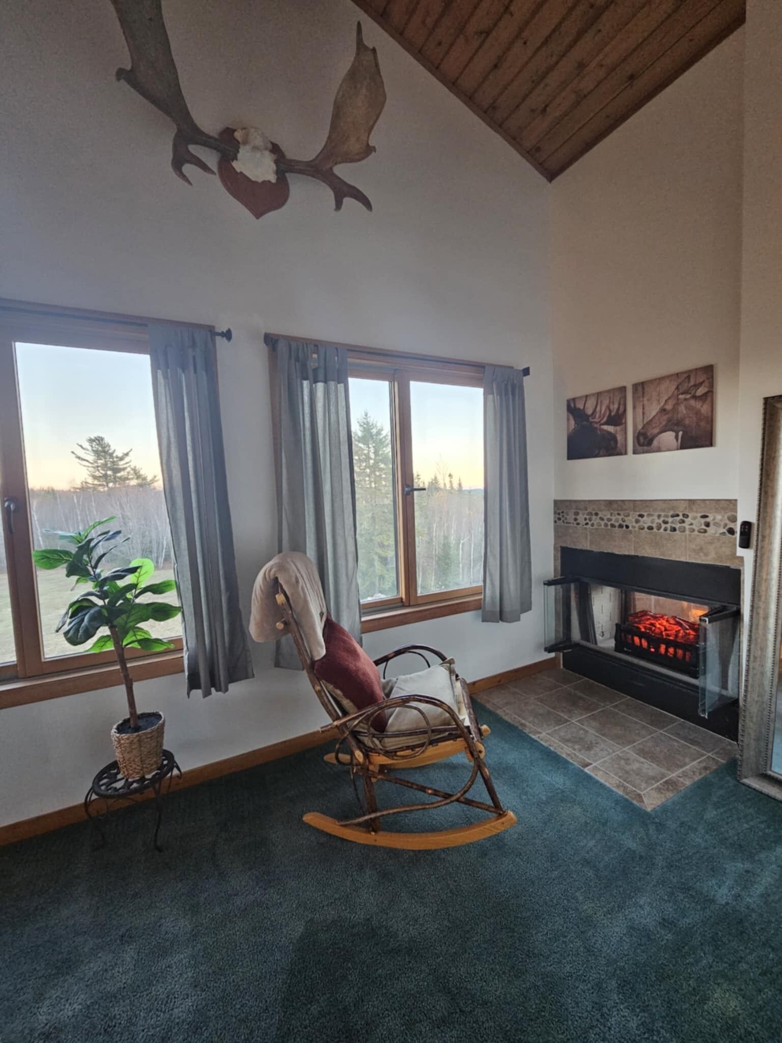 A cozy room with a rocking chair, a fireplace, and large windows with curtains.