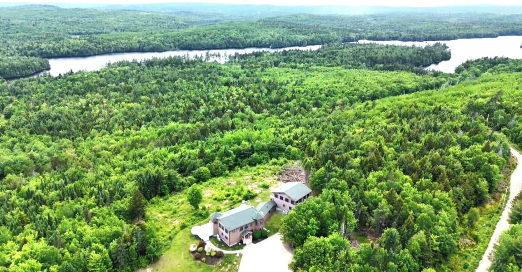Un vaste domaine comprenant une maison principale et une maison d’hôtes, le tout entouré d’une forêt dense et bordé d’un lac.