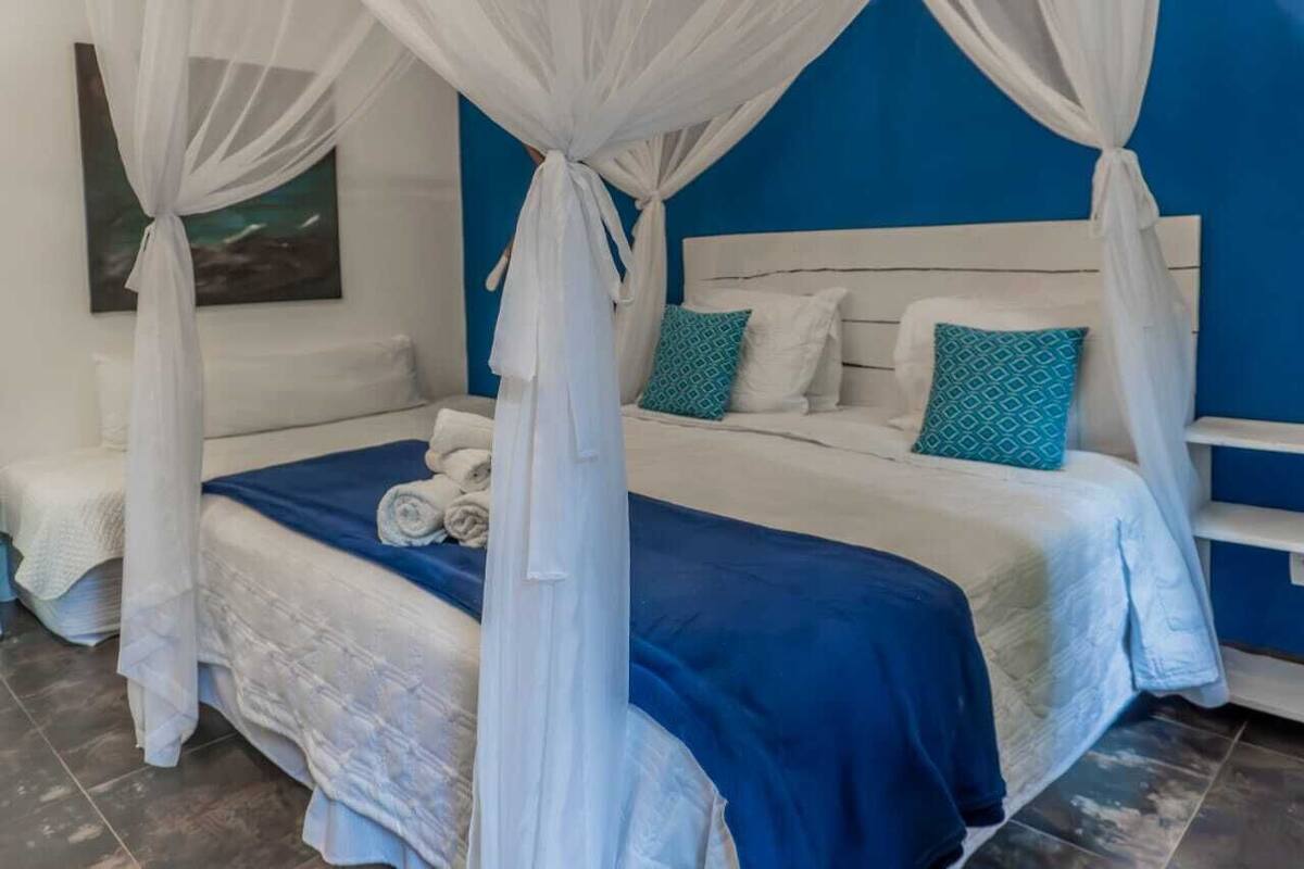 Quarto com cama, dossel branco, paredes azuis e um quadro na parede.
