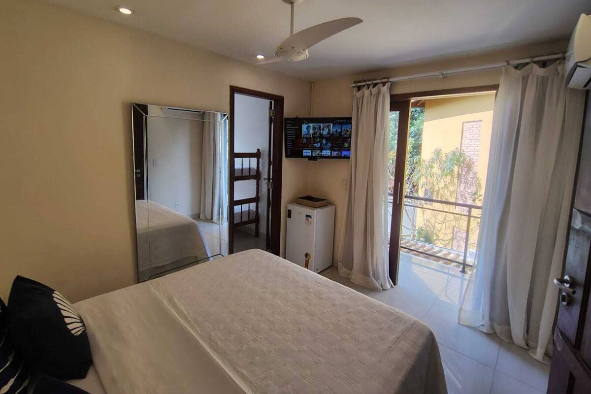 Quarto de hotel com cama, guarda-roupa, televisão na parede e varanda com cortinas.