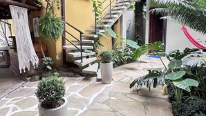Un patio con suelo de piedra, plantas en macetas, una escalera y una hamaca.