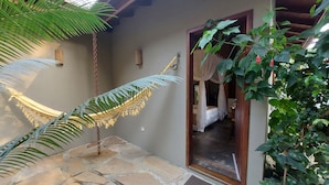 Un patio con suelo de piedra, una hamaca, una cama con dosel y abundante vegetación.