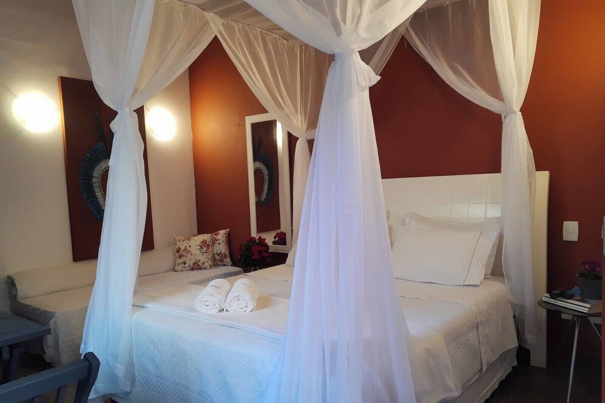 Quarto com cama de dossel, mesa de cabeceira, cadeira e espelho.