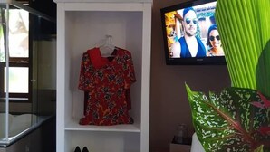 Habitación con un armario blanco que muestra un vestido rojo y zapatos, un televisor y una planta verde grande.