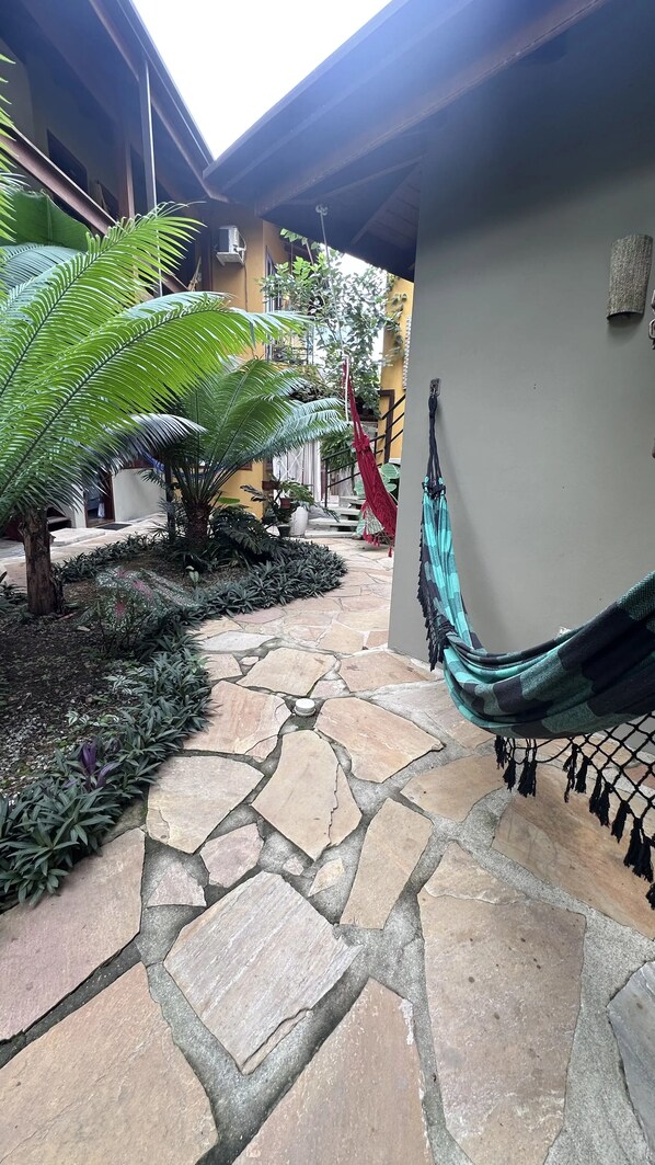 A stone-paved courtyard with a hammock, potted plants, and a building in the background. - Pousada Magias de Paraty (Paraty)