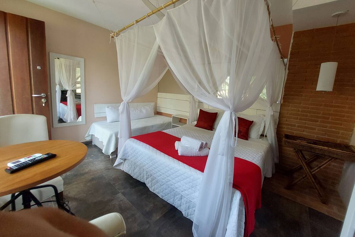 Quarto de hotel com duas camas, uma mesa de madeira, uma cadeira, um espelho e um ventilador de teto.
