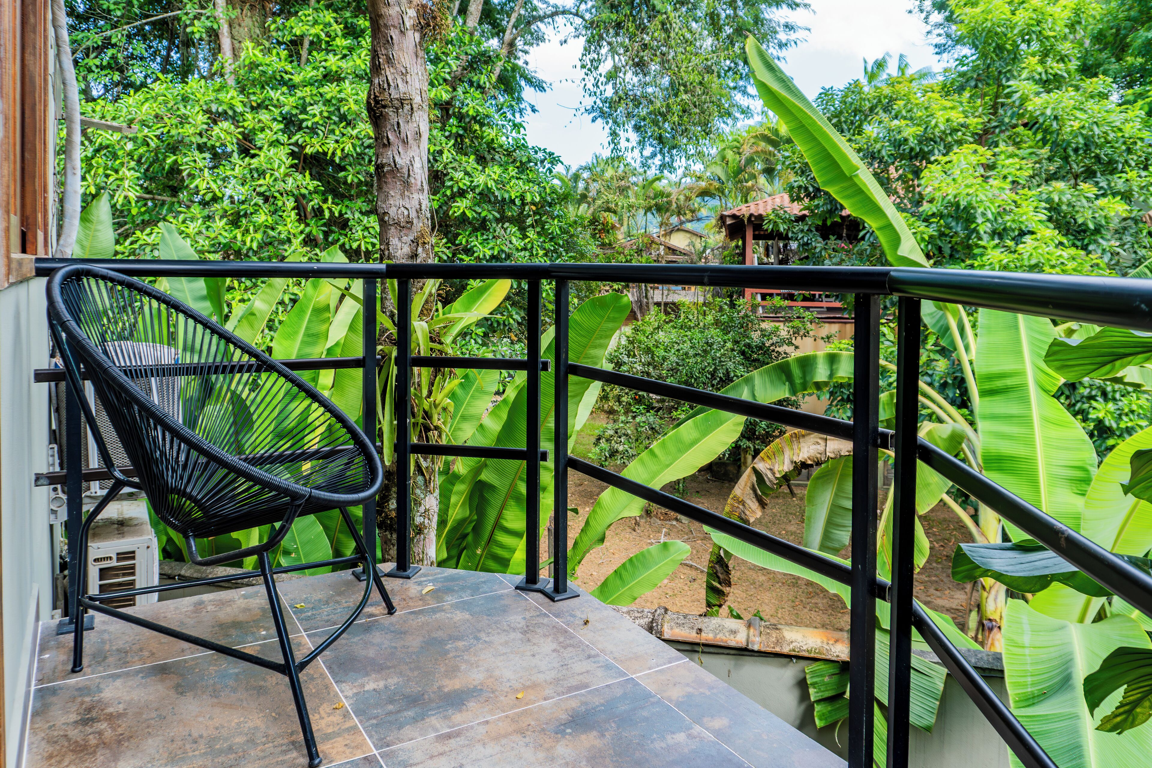 A balcony with a black chair, surrounded by lush green foliage and a tiled floor.