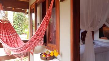 A room with a hammock, a bed with a canopy, and a fruit bowl with a drink on a table.