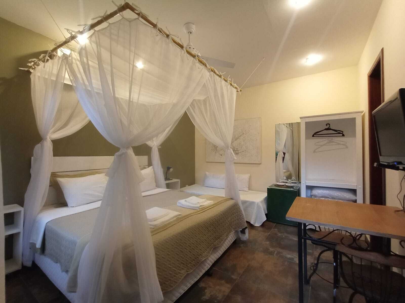 Een slaapkamer met een hemelbed, nachtkastje, televisie en een klein tafeltje.