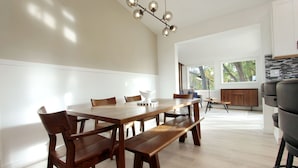 A modern dining area with a wooden table, benches, and a hanging light fixture. - Modern Home with Game Room, Private Yard, Panoramic Views, 5B Sleeps 8+ (Spokane)