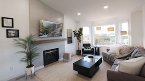 A modern living room with a fireplace, a large window with curtains, a sofa, and a coffee table. - Modern Home with Game Room, Private Yard, Panoramic Views, 5B Sleeps 8+ (Spokane)