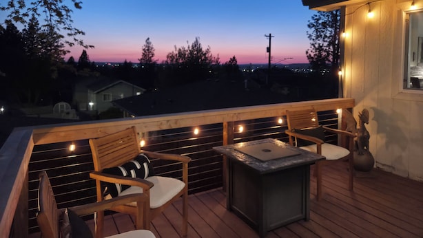 A wooden deck with outdoor seating, a stone table, and string lights. - Modern Home with Game Room, Private Yard, Panoramic Views, 5B Sleeps 8+ (Spokane)
