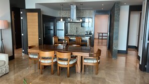 A modern dining area with a wooden table and chairs, a kitchen in the background, and a hallway leading to other rooms.