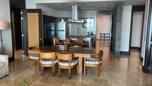 A spacious dining area with a wooden table and chairs, a kitchen in the background, and a modern interior design.
