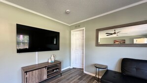 Un salon avec un téléviseur à écran plat, un meuble en bois, un canapé noir et un tapis à motifs.