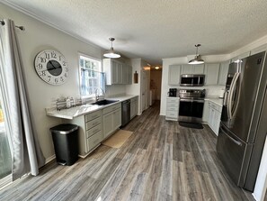 A modern kitchen with stainless steel appliances, a large window, and a clock on the wall. - Hot Tub, Pet Friendly, 3 miles to Emerald Isle, fully fenced yard. (Newport)