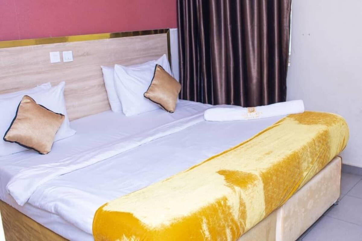 A hotel room with a bed, white bedding, a yellow throw blanket, and brown curtains.