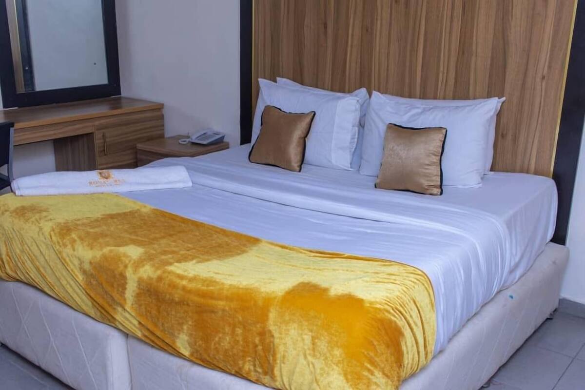 A neatly made bed with white and brown pillows, a yellow blanket, and a wooden headboard.