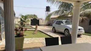 A covered patio area with a table and chairs, a white car parked outside, and a water tank in the background. - Apartment with View and Balcony B (Kunkajan-Jataya)