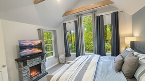 Ein Schlafzimmer mit Kamin aus Stein, einem Bett mit gestreifter Bettwäsche, einem Fernseher und großen Fenstern mit Vorhängen.