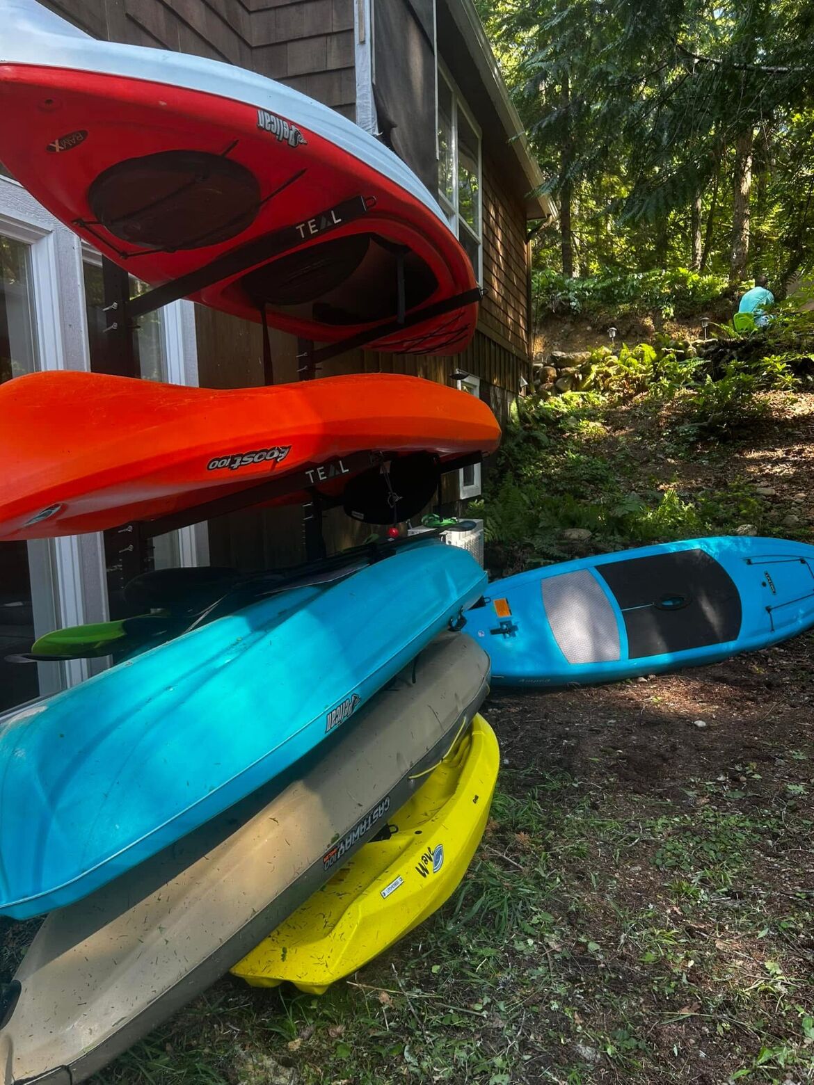 Tres kayaks estacionados frente a una casa con fachada de madera y un jardín.