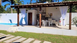 A covered outdoor area with a brick oven, white chairs, and a small table.
